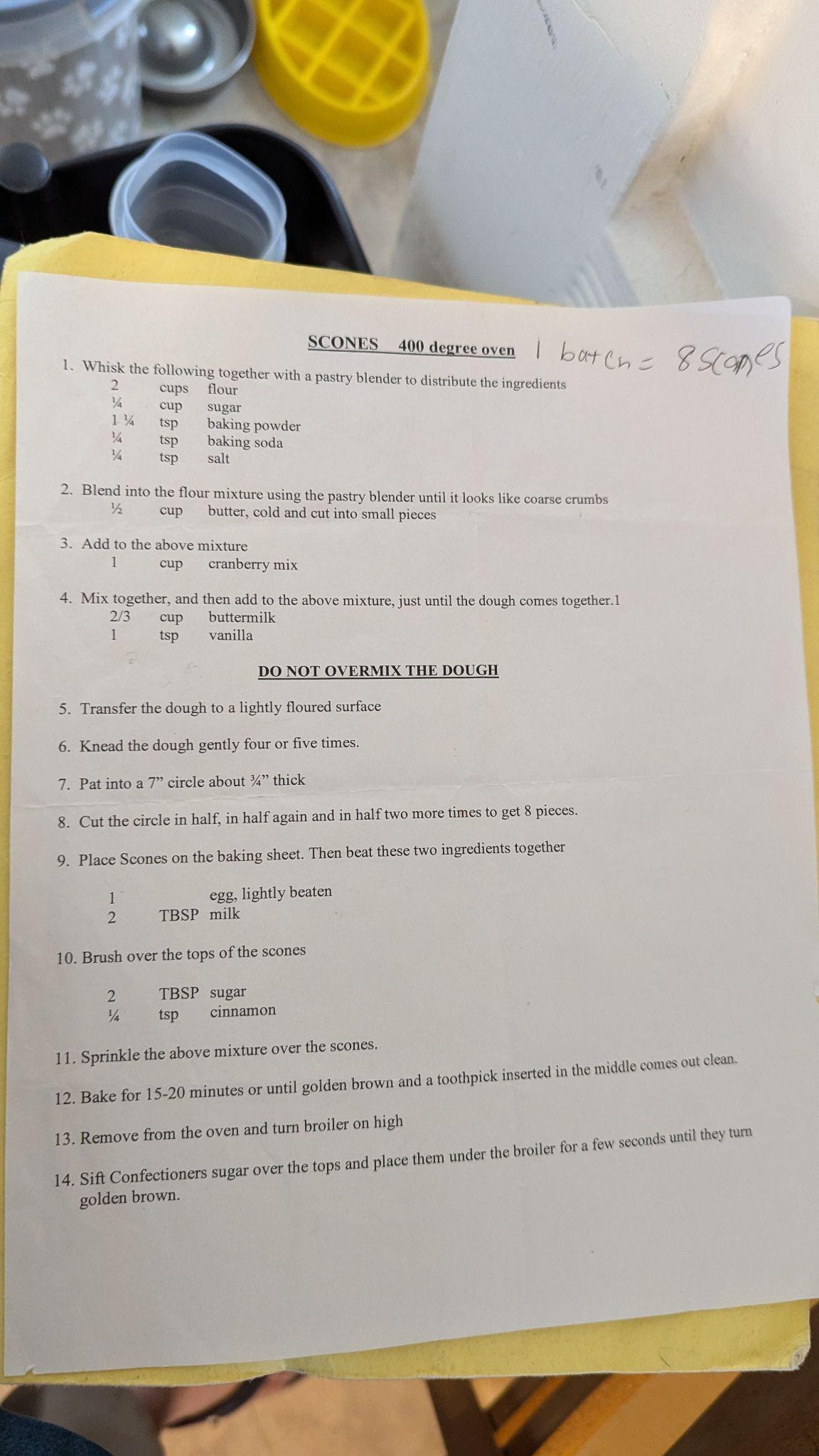 photo of the recipe for chocolate chip scones. It says: 
                    SCONES 400 degree oven |1 batch = 8 scones

                    1. Whisk the following together with a pastry blender to distribute the ingredients
                    2 cups flower
                    1/4 cup sugar
                    1 & 1/4 tsp baking powder
                    1/4 tsp baking soda
                    1/4 tsp salt
                    
                    2. Blend into the flour mixture using the pastry blender until it looks like coarse crumbs
                    1/2 cup butter, cold and cut into small pieces
                    
                    3. Add to the above mixture
                    1 cup cranberry mix (or in this case chocolate chips)
                    4. Mix together, and then add to the above mixture, just until the dough comes together.1
                    2/3 cup buttermilk
                    1 tsp vanilla
                    
                    DO NOT OVERMIX THE DOUGH
                    
                    5. Transfer the dough to a lightly floured surface
                    
                    6. Knead the dough gently four or five times.
                    
                    7. Pat into a 7 inch circle about 3/4 inch thick
                    
                    8. Cut the circle in half, in half again and in half two more times to get 8 pieces.
                    
                    9. Place Scones on the baking sheet. Then beat these two ingredients together
                    1  egg, lightly beaten
                    2 TBSP Milk
                    
                    10. Brush over the tops of the scones
                    2 TBSP sugar
                    1/4 tsp cinnamon
                    
                    11. Sprinkle the above mixture over the scones.
                    12. Bake for 15-20 minutes or until golden brown and a toothpick inserted in the middle comes out clean.
                    13. Remove from the oven and turn broiler on high
                    14. Sift Confectioners sugar over the tops and place them under the broiler for a few seconds until they turn golden brown.
                    